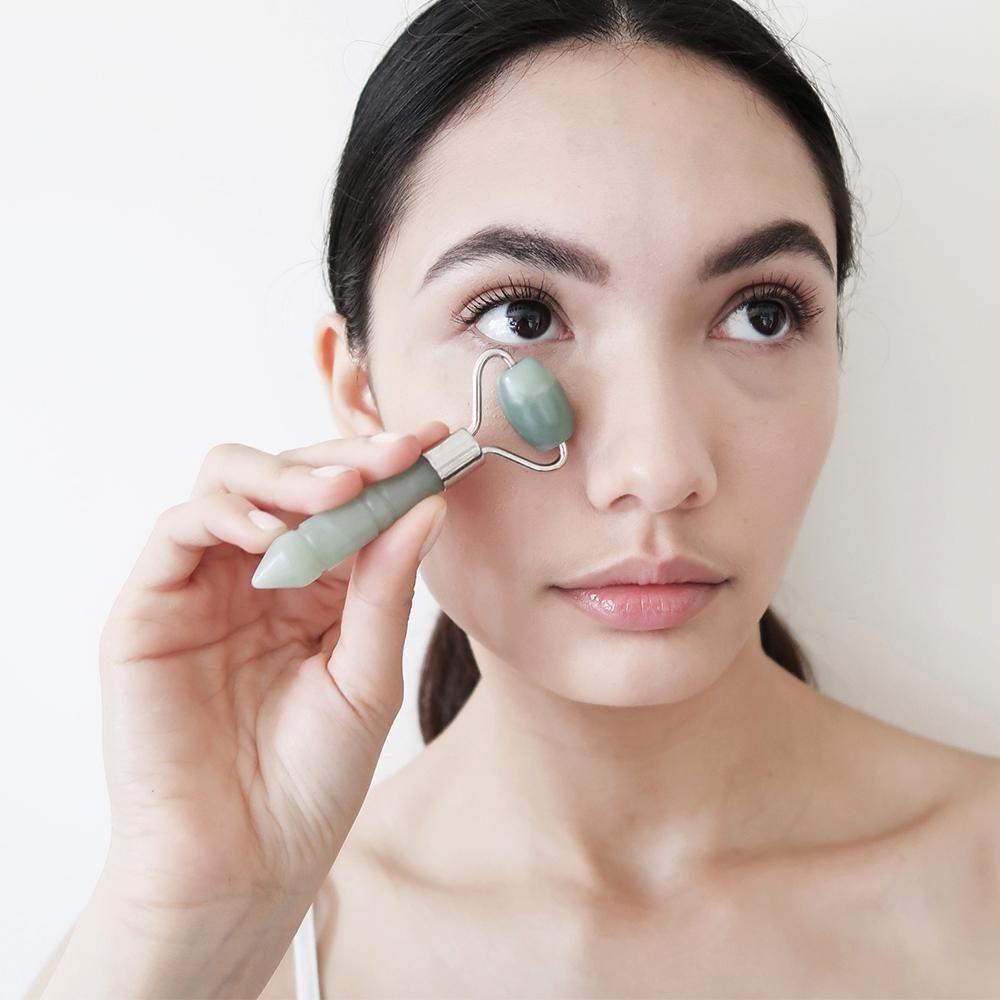 Woman running jade roller across her cheek